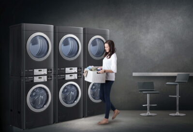 A photo of a woman holding a laundry basket standing in front of LG Commercial Laundry machines set up in a laundromat