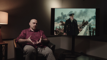 A photo of a man sitting infront of a screen with a movie playing