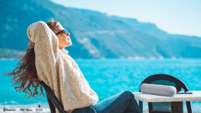 A woman listens to music on her LG StanbyME Speaker while relaxing by the ocean