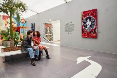 A couple discusses Shepard's artwork while sitting in a showroom where arrows painted on the floor indicate viewing directions