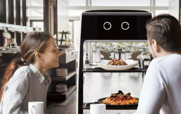 A picture of a man and a woman waiting to receive their food from the LG CLOi bot