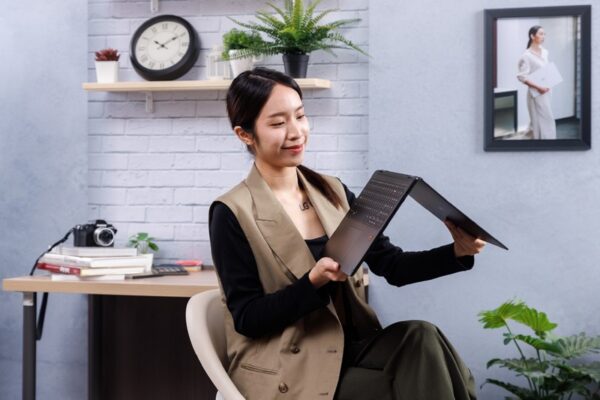 A woman is sitting down while holding the LG gram folded