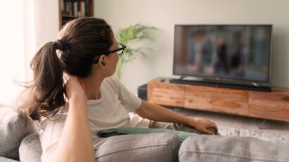 A woman is watching TV on a sofa while listening through T90S earbuds