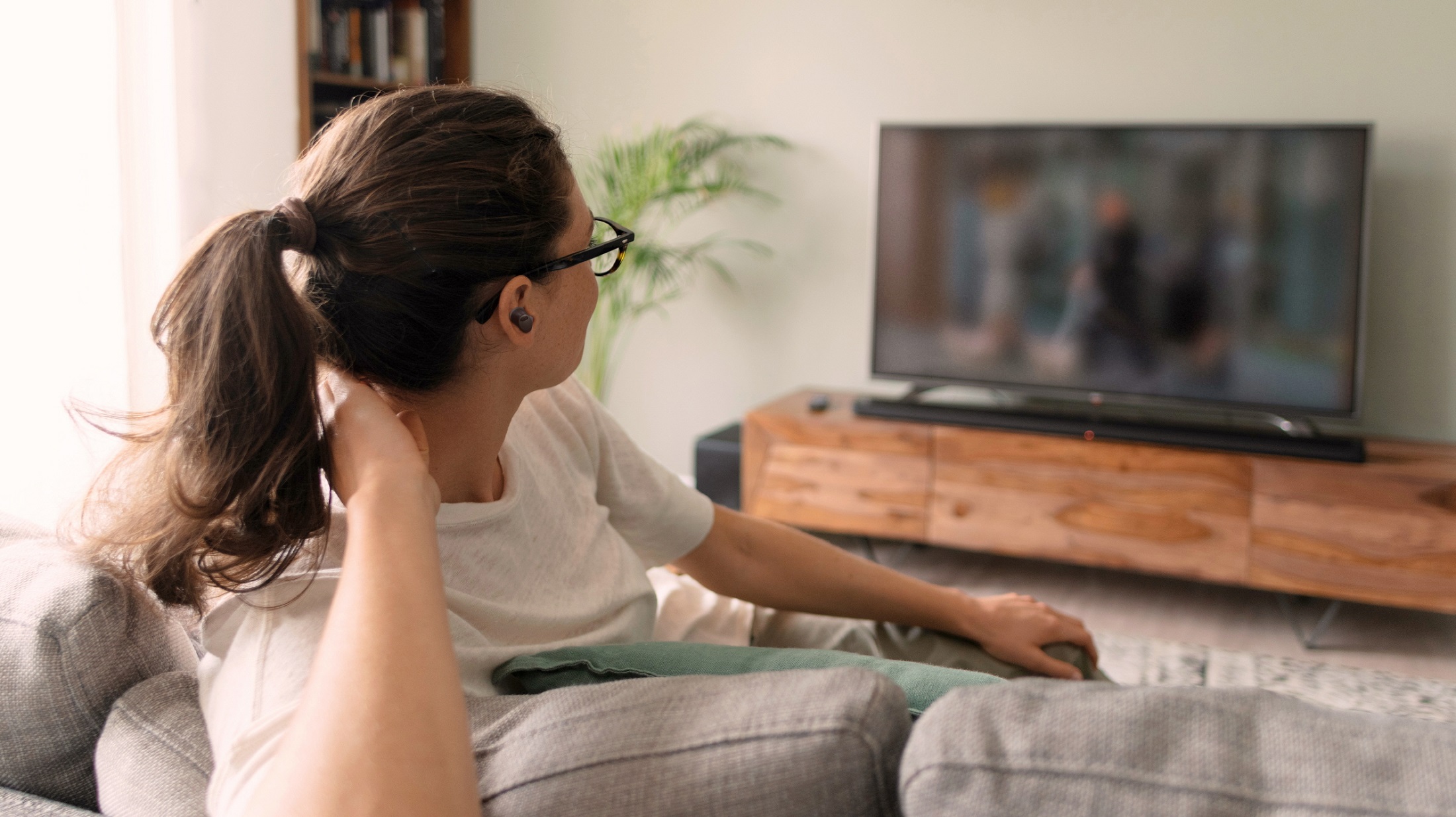A woman is watching TV on a sofa while listening through T90S earbuds