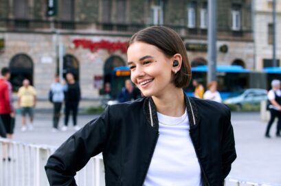 A woman wearing T90S earbuds is standing in the middle of a plaza with a big smile on her face