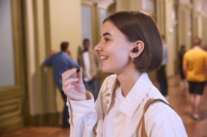 A woman standing in a crowded hallway is putting in T90S earbuds