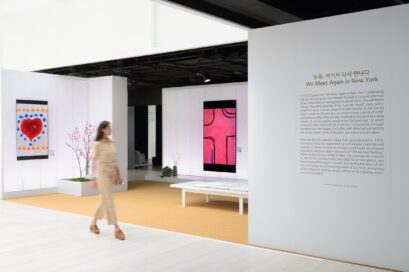 A woman is walking past Kim Whanki’s artwork toward a wall of exhibit information titled “We Meet Again In New York