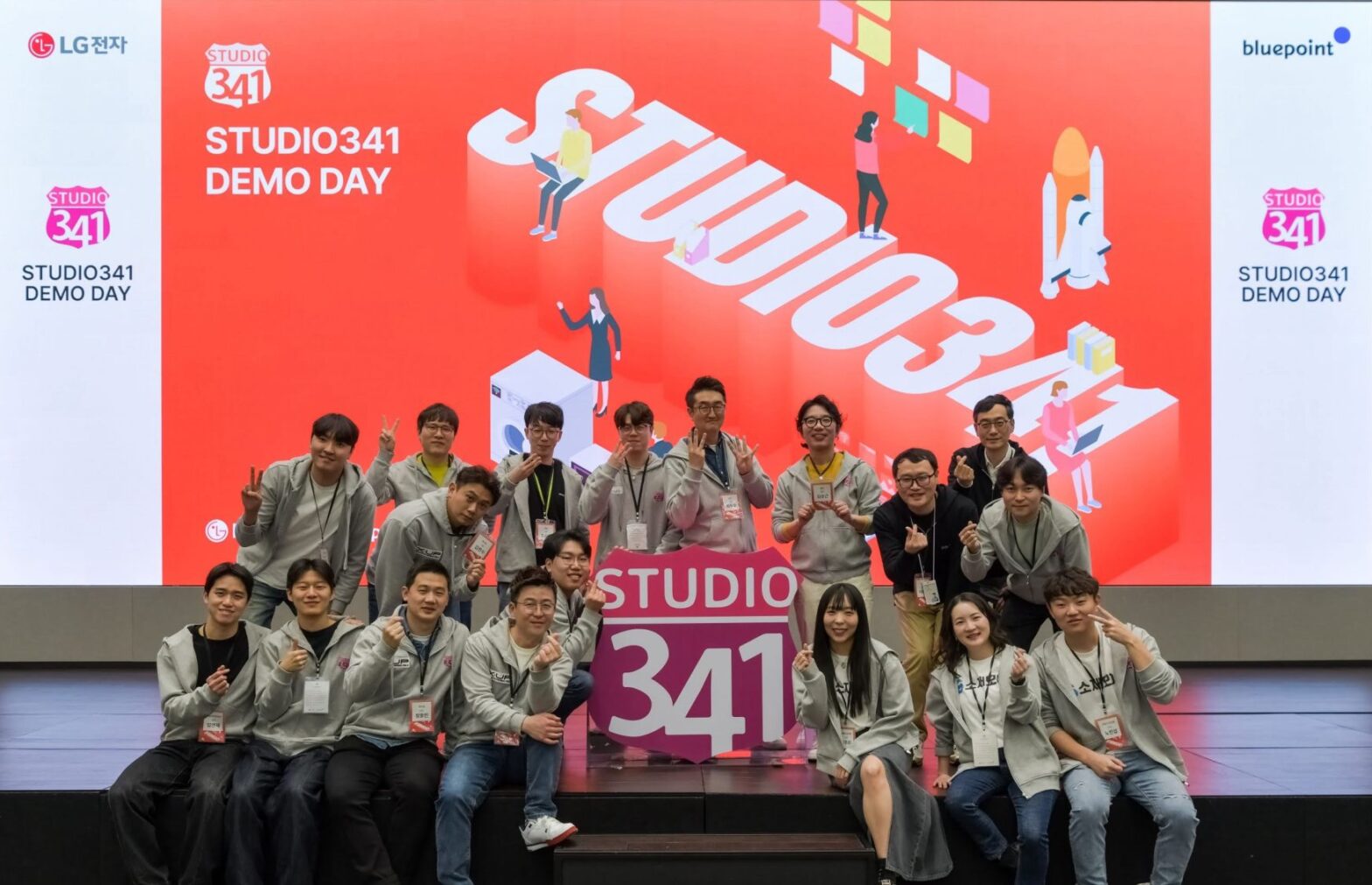 A picture of people sitting, smiling, and posing together on stage at a demo day event of STUDIO341.