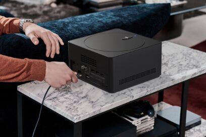 A man is connecting a cable to a Zero Connect Box, which sits on a side table that hides video games and controllers underneath