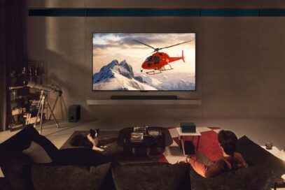 A man is watching a helicopter on the screen of a wall-mounted LG OLED M4, with a wireless Zero Connect Box sitting on a small table in the living space
