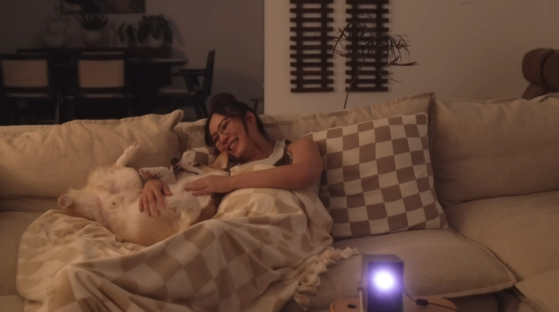 A woman is relaxing on a couch with the LG CineBeam Q projector in front of her