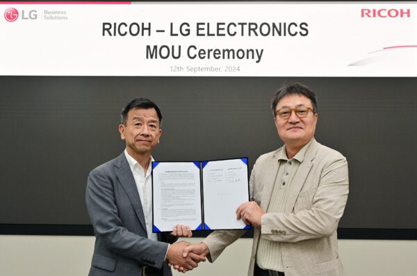 Representatives from LG (left) and Ricoh (right) shake hands while holding a signed MOU