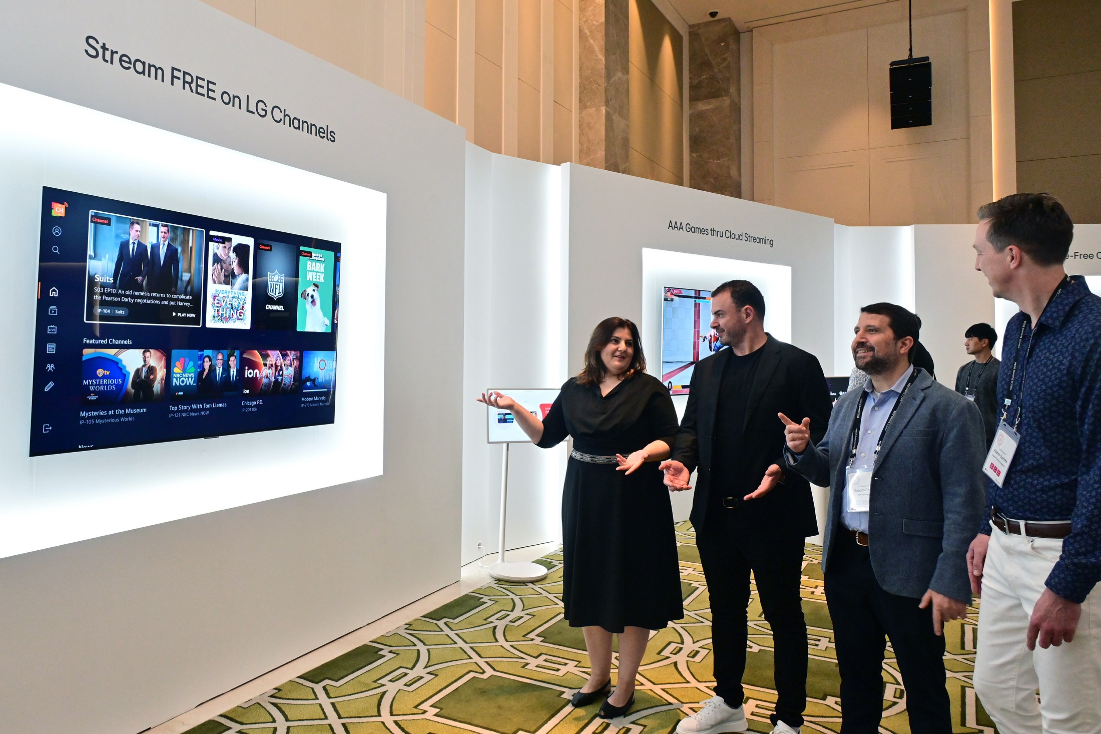 A group of attendees are exploring webOS content on a wall-mounted LG smart TV at webOS Summit 2024