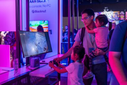 A father is helping his two daughters explore games on LG smart devices set up in LG’s Gaming Zone