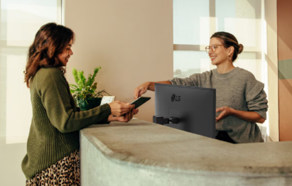 A woman assists another woman at the counter, with the LG Business Monitor positioned between them