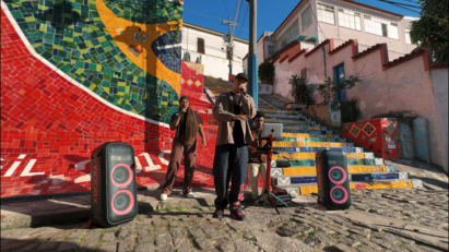 A group of three street performers in Brazil deliver a vibrant performance in front of a colorful mosaic mural and staircase, accompanied by two LG XBOOM speakers