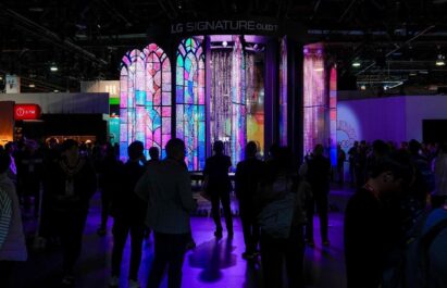 A photo of a stunning kinetic media façade made of 28 transparent slim OLED screens glowing in the dark and the people watching them