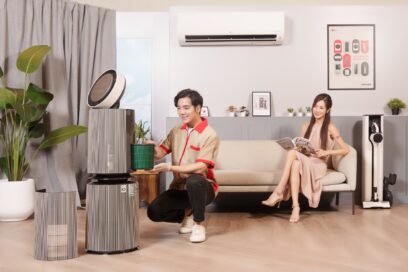 A photo of a woman sitting on a couch in a showroom with LG products and a man next to an LG PuriCare