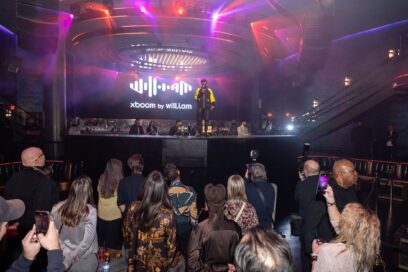 A photo will.i.am holding a microphone on stage and the crowd watching him