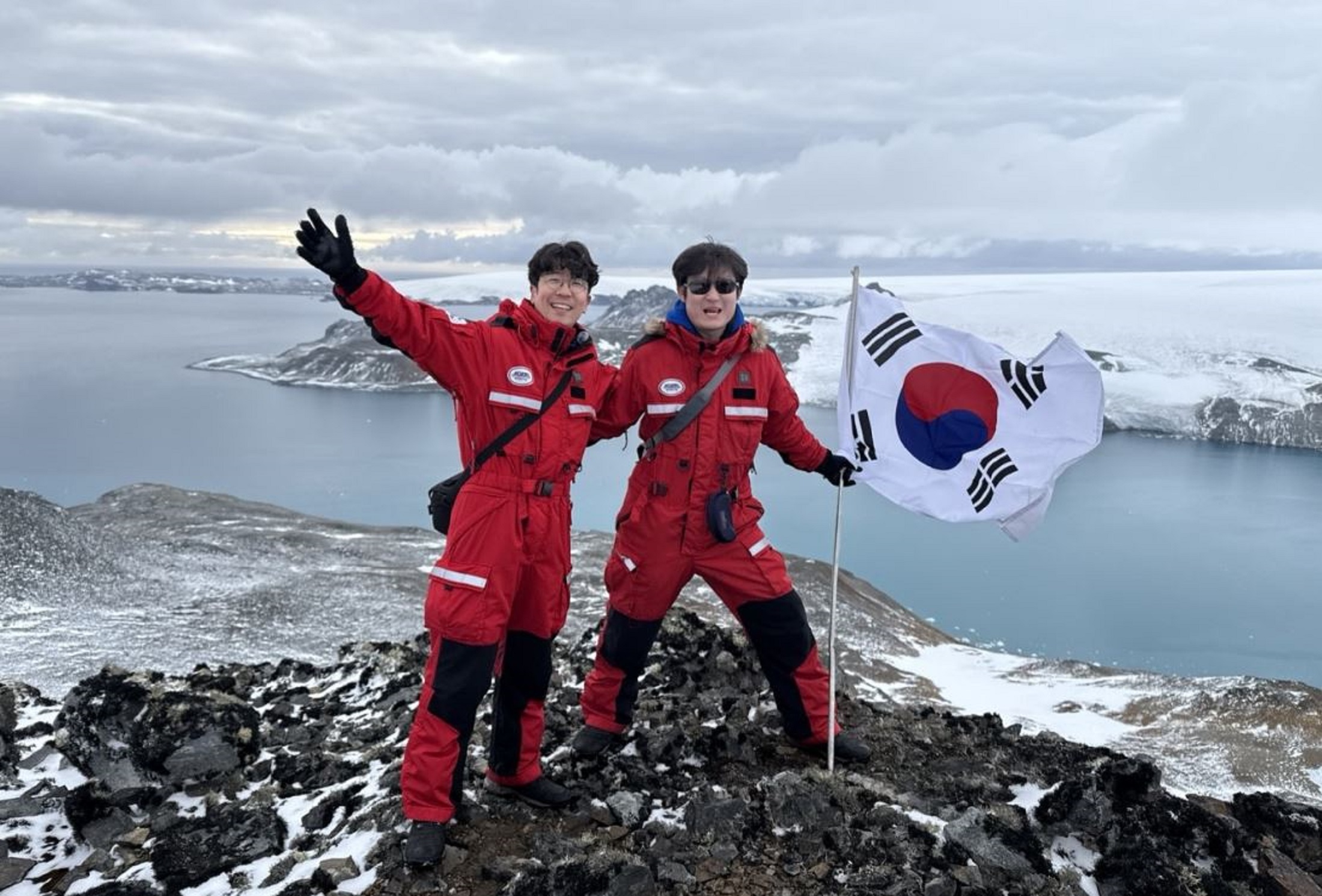 A photo of two men on top of a mountain with a Korean flag